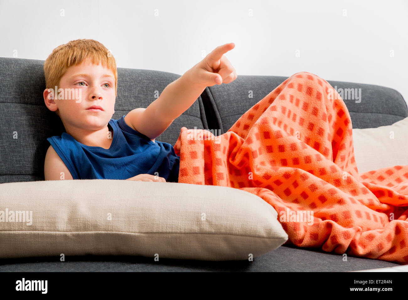 Young, red haired boy of seven lounging on the sofa indoors Stock Photo