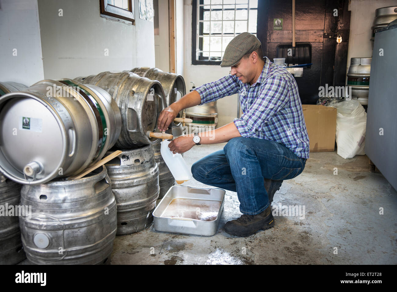 A brewer pouring beer from a barrel in a small brewery in Hampshire UK Stock Photo