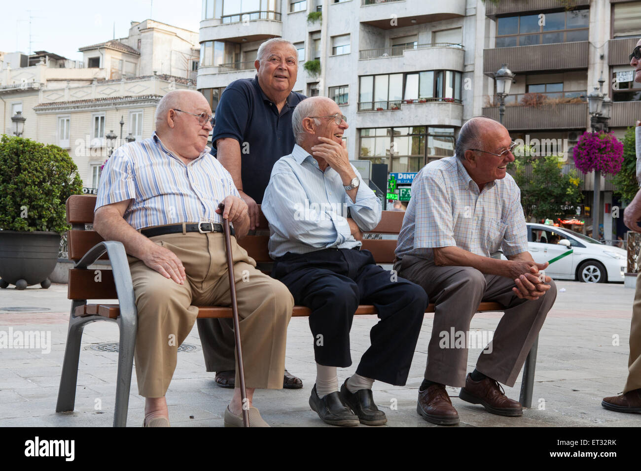 A group of men enjoying an evening get-together on a bench in Puerta Real in Granada Stock Photo