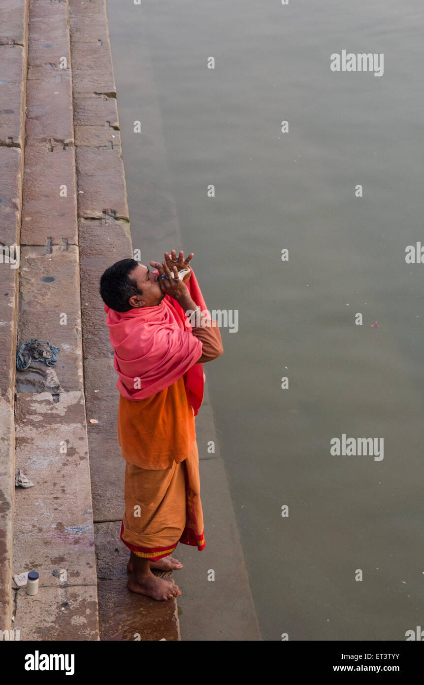 A worshiper blows a horn on the banks of the Ganges at Varanasi Stock Photo