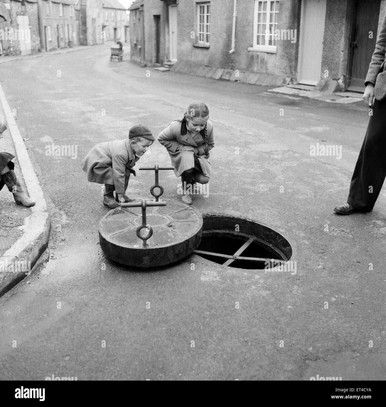 Children looking down a drain hole in the road in Thornbury, South Gloucestershire. 2nd November 1954 Stock Photo