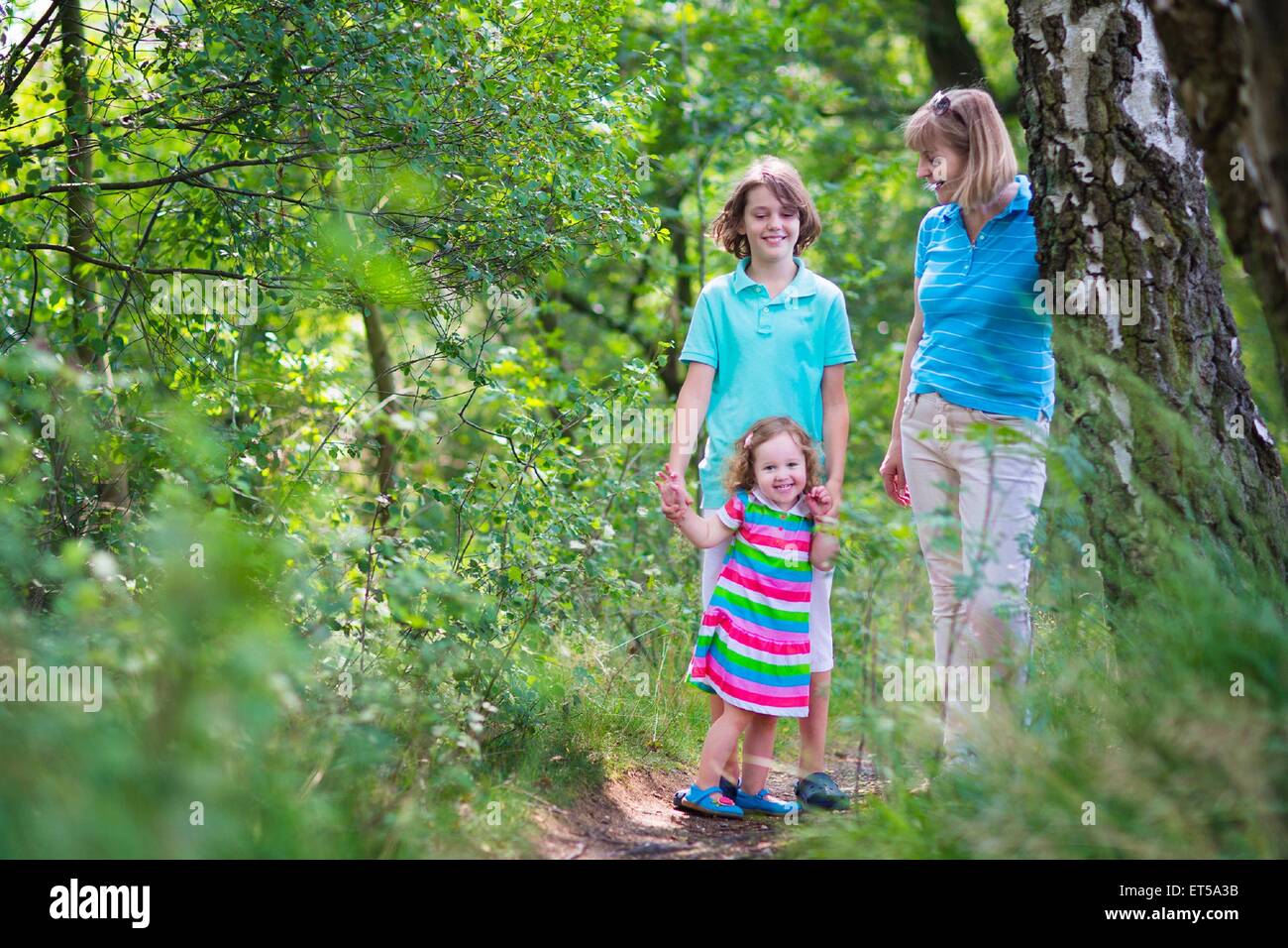 Happy active woman enjoying hiking with two children, school age boy and cute curly toddler girl walking together in a beautiful Stock Photo