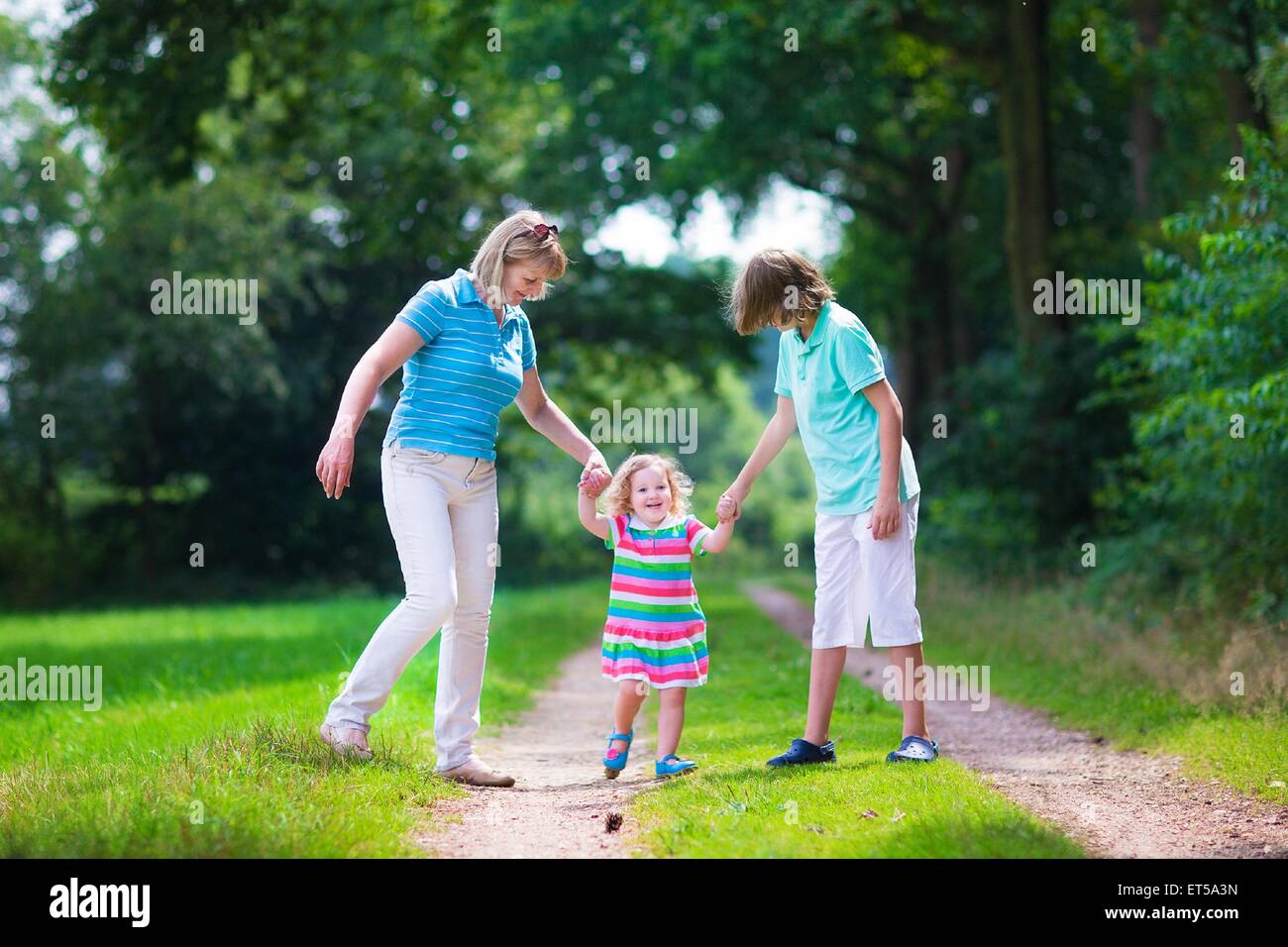 Happy active woman enjoying hiking with two children, school age boy and cute curly toddler girl walking in pine wood forest Stock Photo