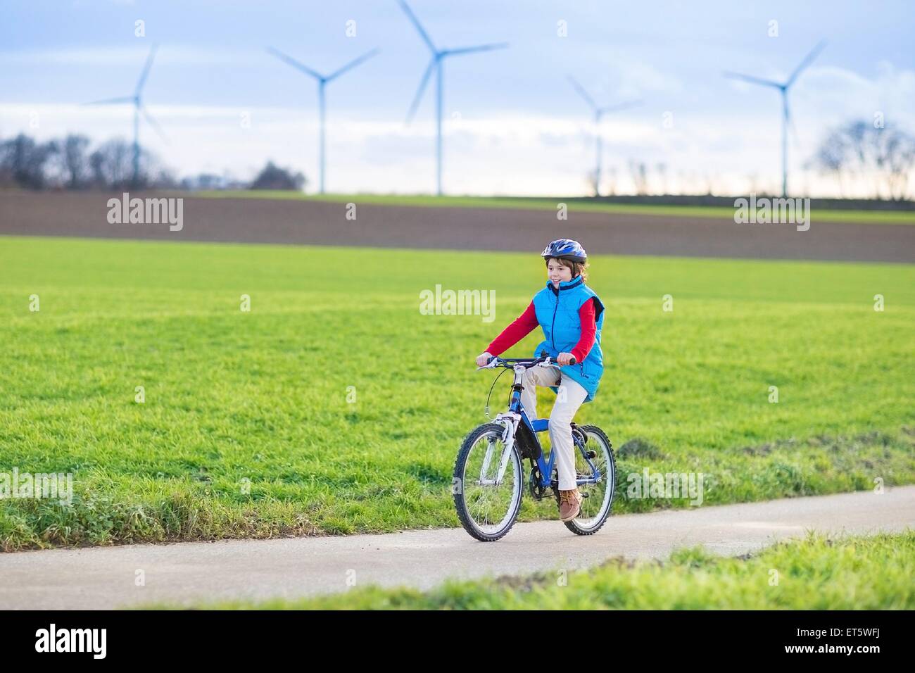 Happy young teenager boy riding his bike in a beautiful European landscape with energy wind mills Stock Photo