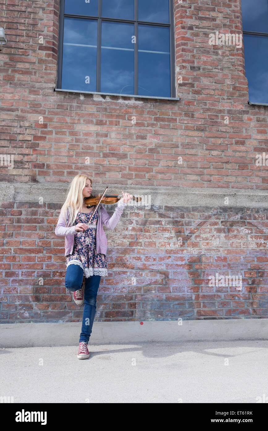 Caucasian teenage girl playing violin in front of brick wall, Munich ...