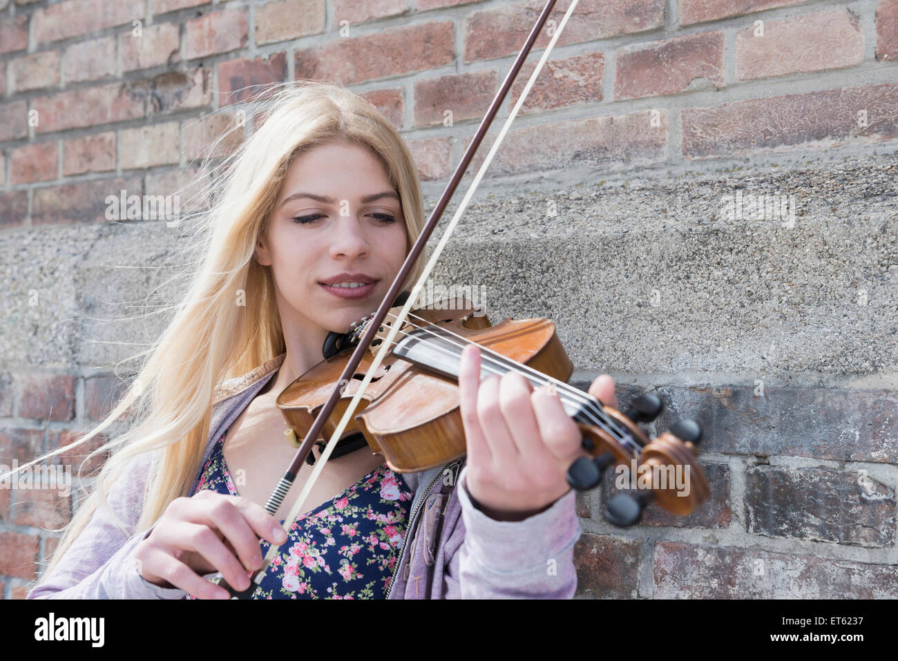 Caucasian teenage girl playing violin in front of brick wall, Munich ...