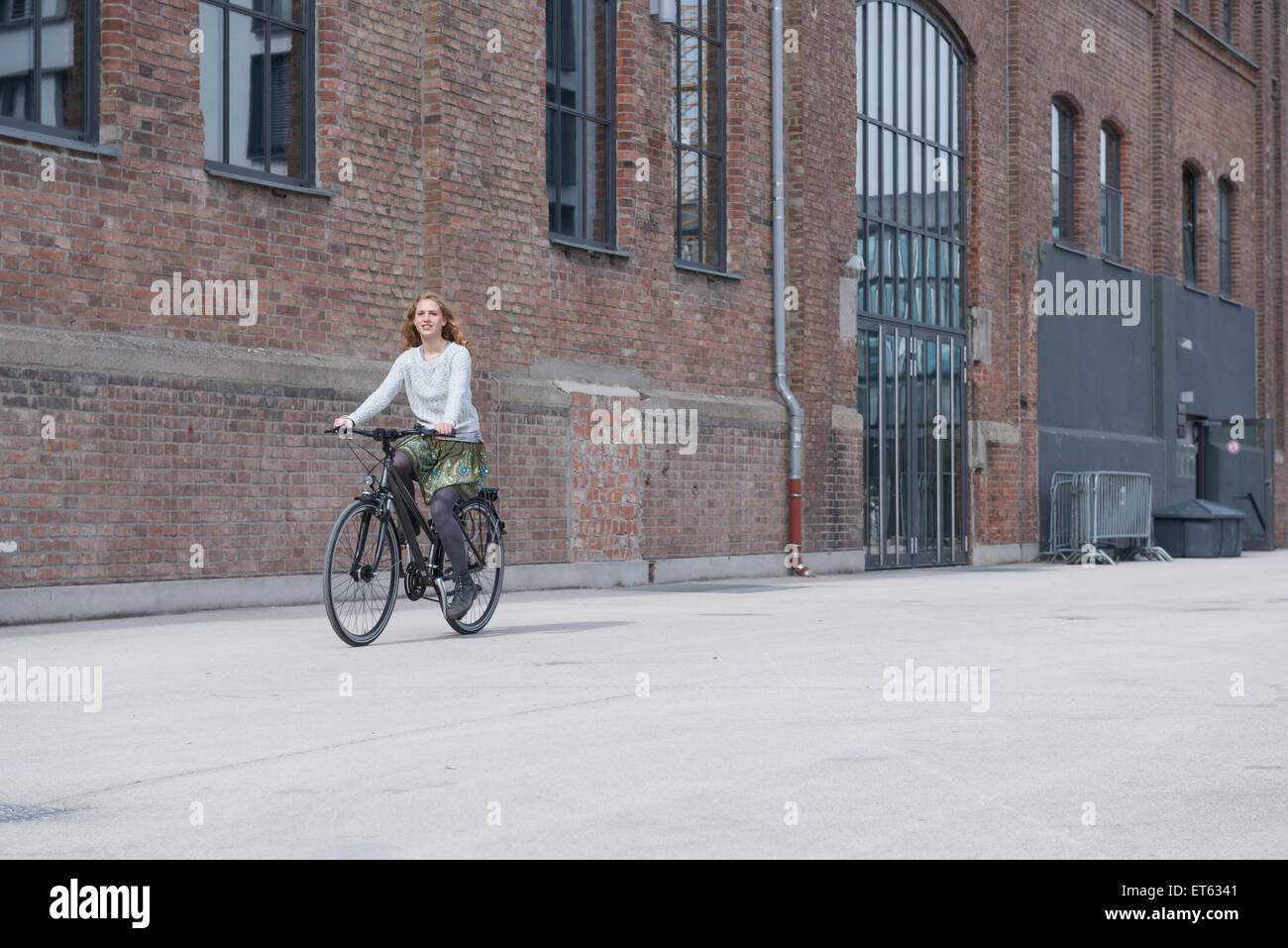 Young woman riding a bicycle in front of brick wall, Munich, Bavaria