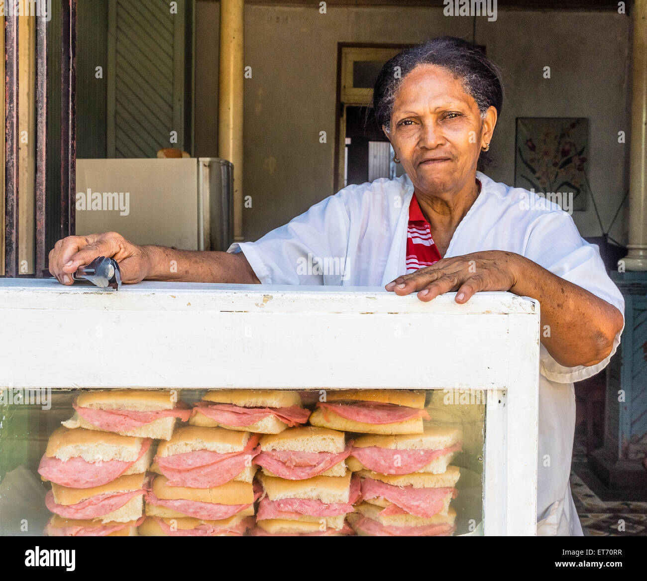A older AfroCuban female sandwich vendor leans on her display case