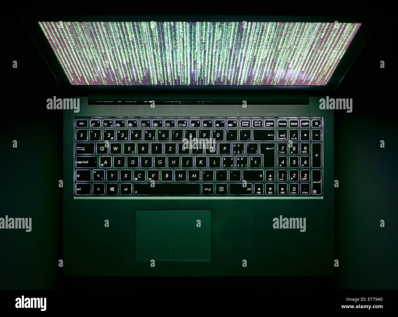 A laptop computer in the dark with illuminated keyboard and mystic program code on screen Stock Photo