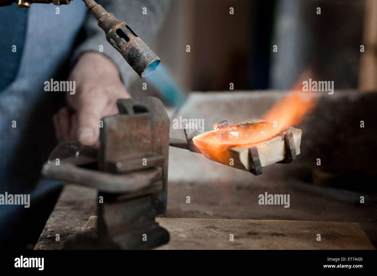 Senior male goldsmith melting and casting with blow torch at