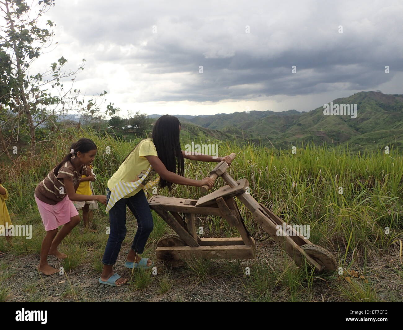 Zamboanga del Sur, Philippines. 12th June, 2015. Young girls playing and enjoying a wooden bicycle on the rough roads of Sitio Lumangking in Dumingag, Zamboanga del Sur which is considered as 'World Day Against Child Labor. Around the world, there are 120 million children between the ages of 5 and 14 are involved in child labor, with boys and girls in this age group almost equally affected. Credit:  Sherbien Dacalanio/Pacific Press/Alamy Live News Stock Photo