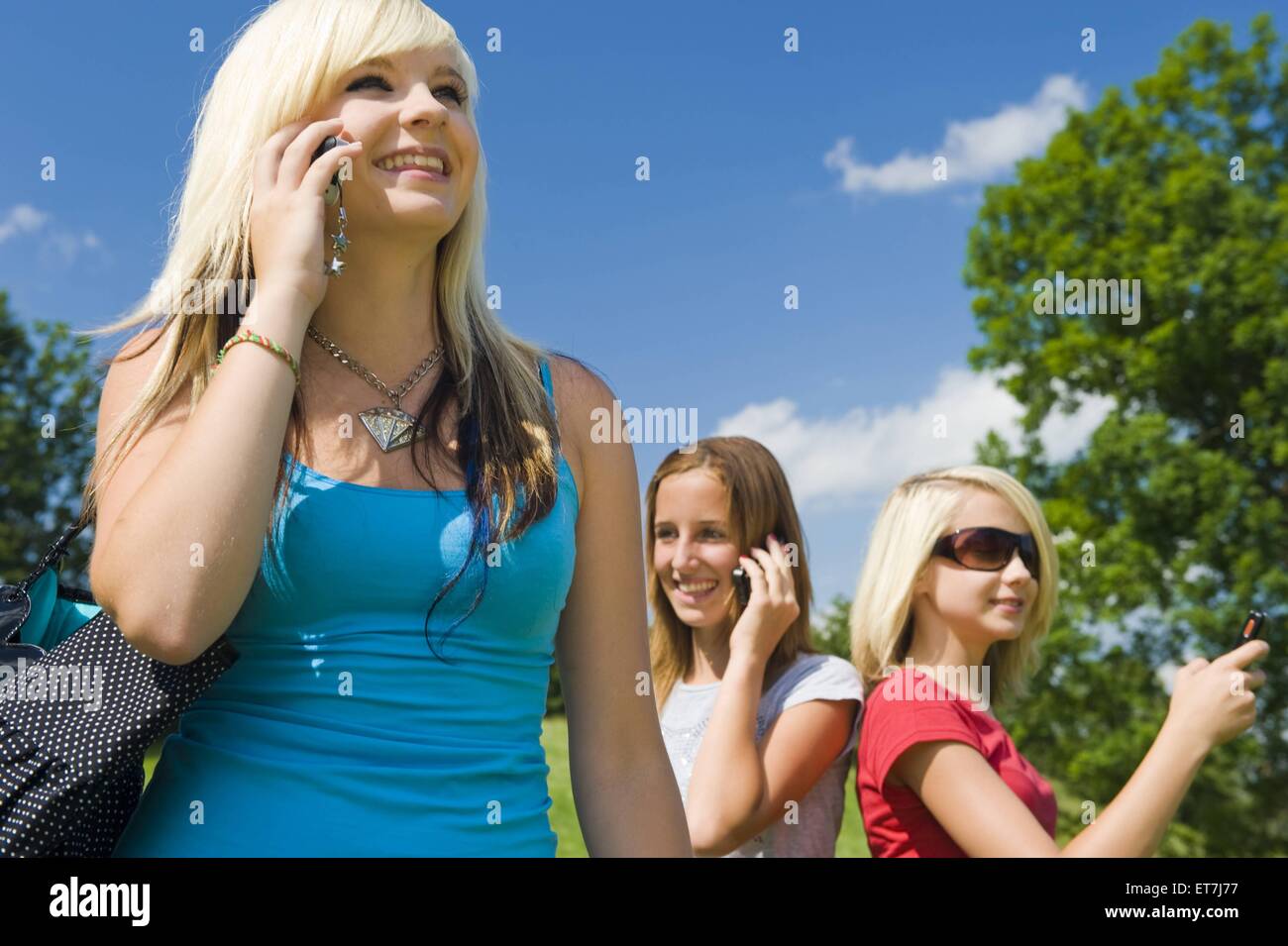 drei junge Maedchen stehen auf einer Wiese und telefonieren laechelnd mit dem Handy | three young girls standing in a meadow pho Stock Photo