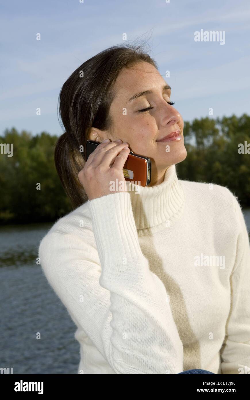 junge Frau am See telefoniert mit dem Handy, Oesterreich | young woman at a lake phoning with a mobile phone, Austria Stock Photo