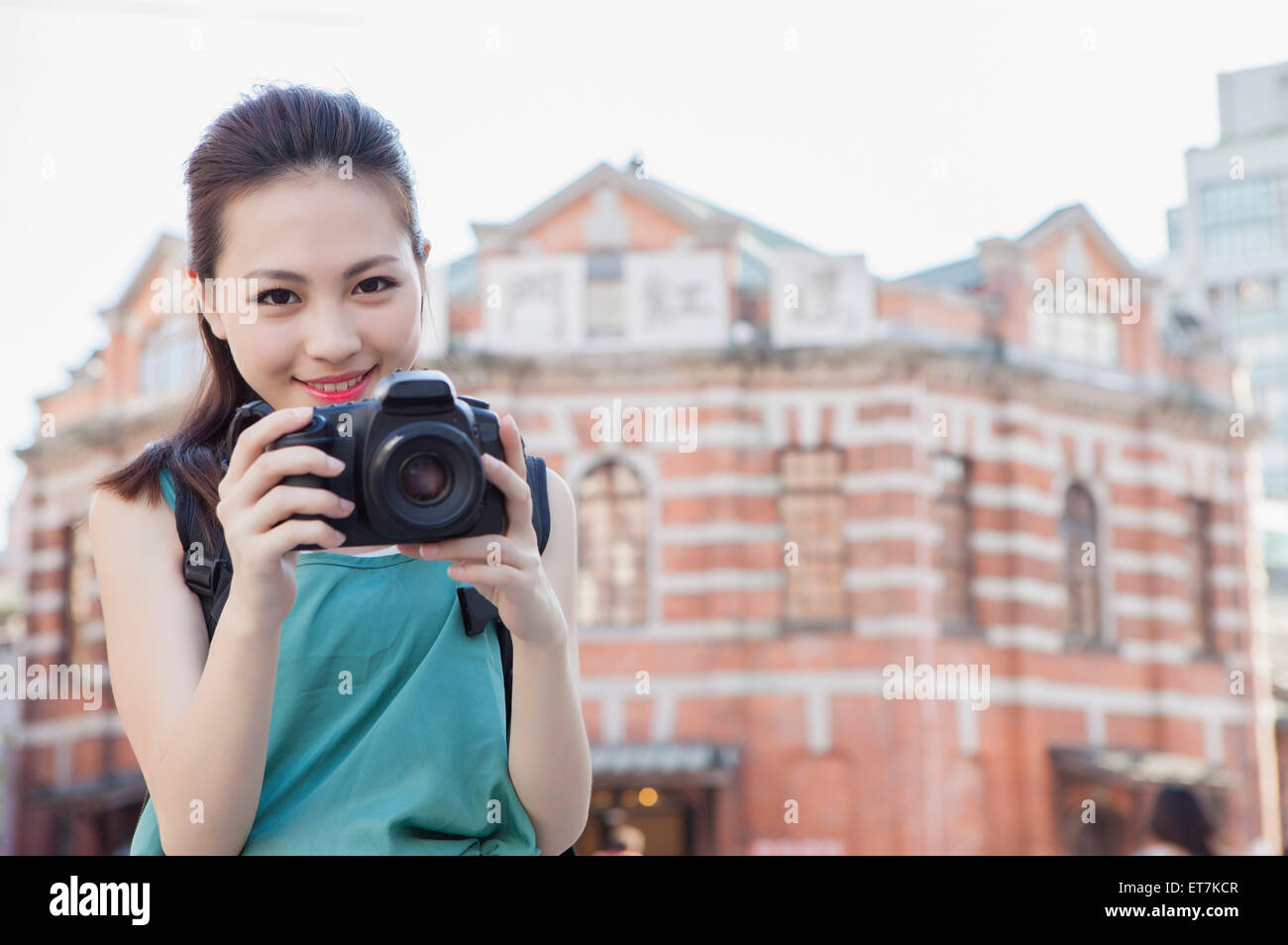 Young woman holding camera and smiling Stock Photo - Alamy