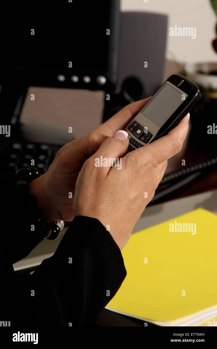 Geschaeftsfrau im Buero, am Schreibtisch sitzend und mit dem Handy eine SMS schreibend | female executive in the office, typing  Stock Photo