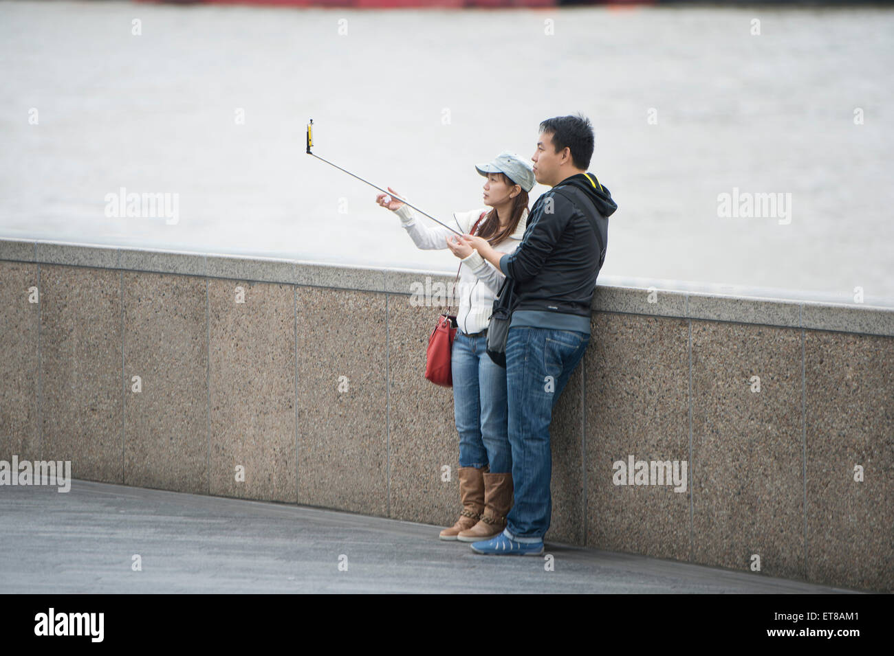 Japanese tourists taking selfie photographs using a selfie stick by the River Thames in London Stock Photo