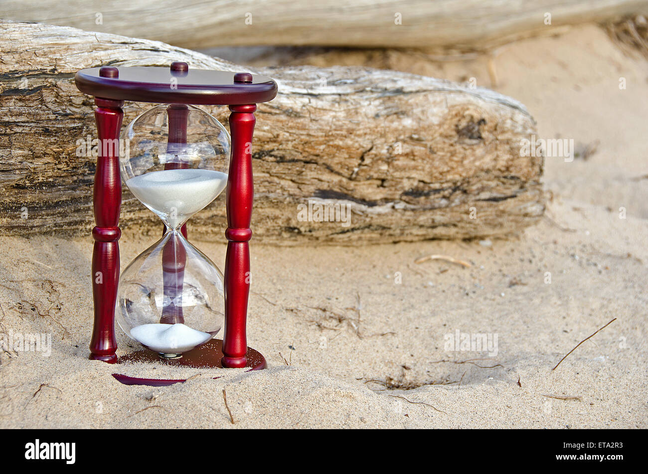 Sand timer in beach sand with driftwood log. Stock Photo