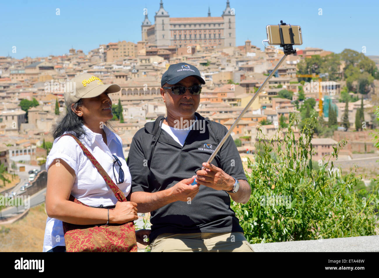 Tourists using a selfie stick and camera phone to take photograph of themselves overlooking Toledo, Spain Stock Photo