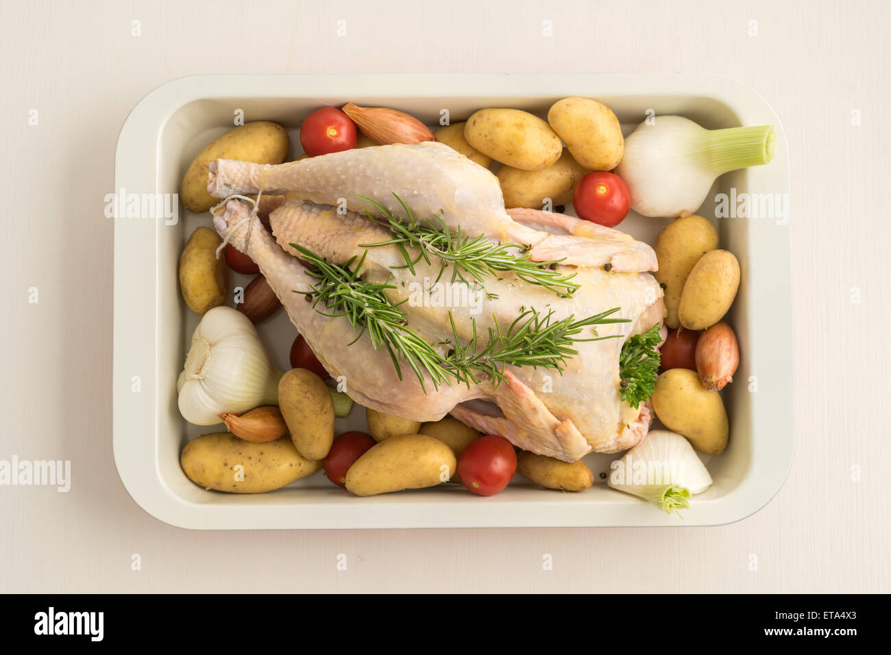 Chicken prepared for roasting with young garlic, shallots, parsley, cherry tomatoes, potatoes and olive oil in a casserole dish Stock Photo