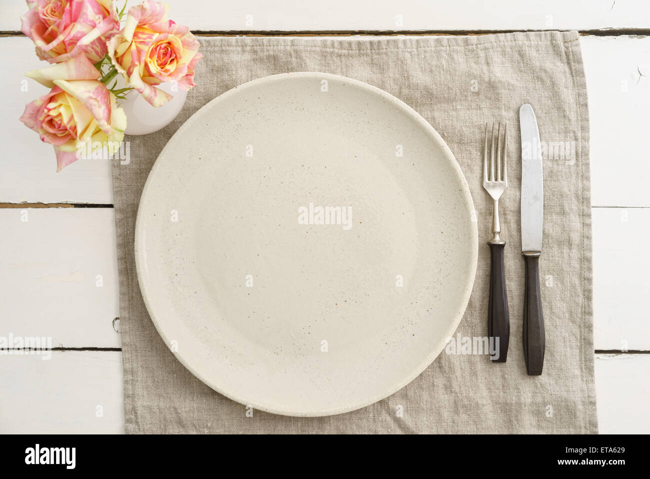 Empty beige plate with vintage silverware on linen cloth with roses Stock Photo