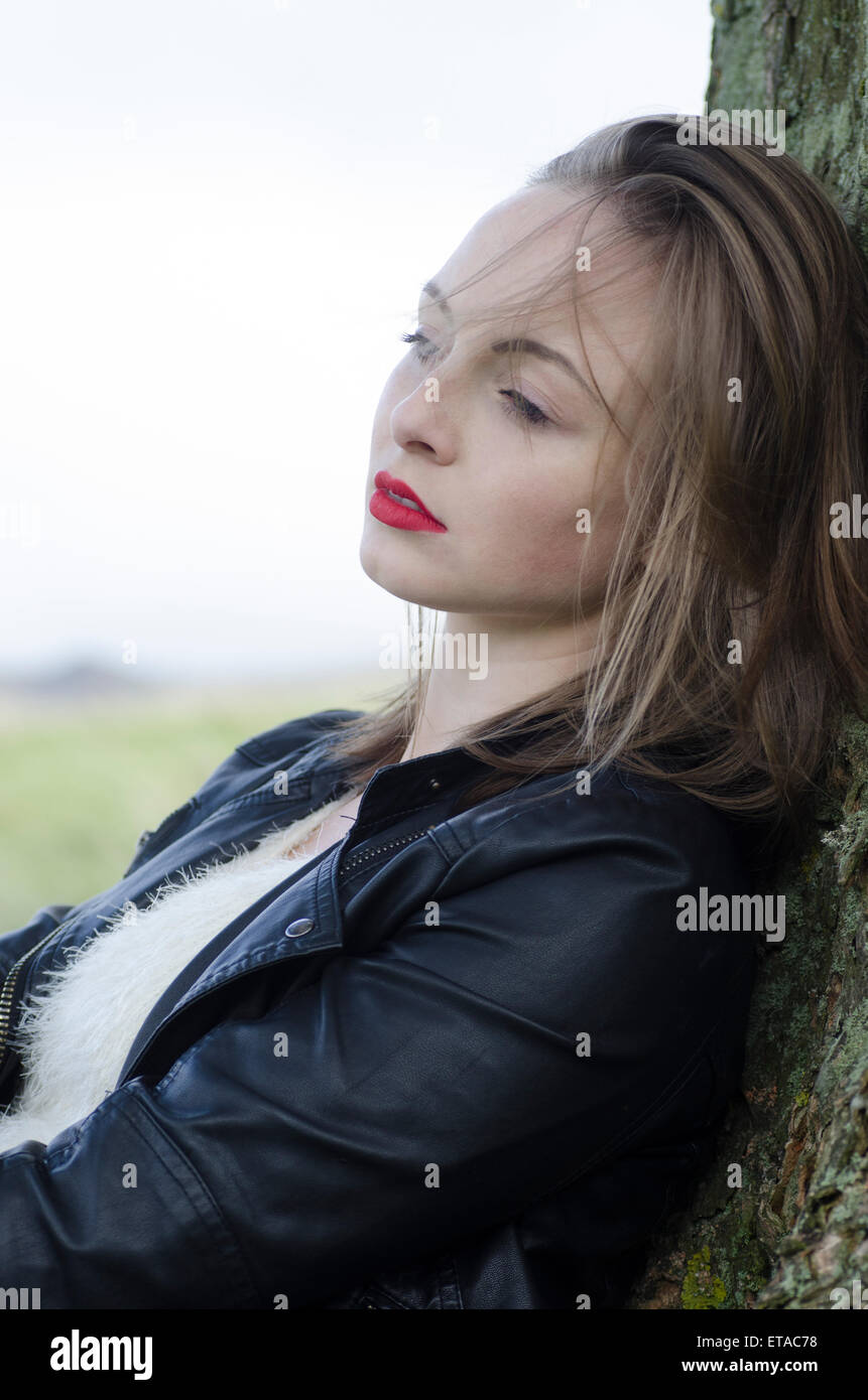 Sad young woman leaning against a tree in the countryside Stock Photo
