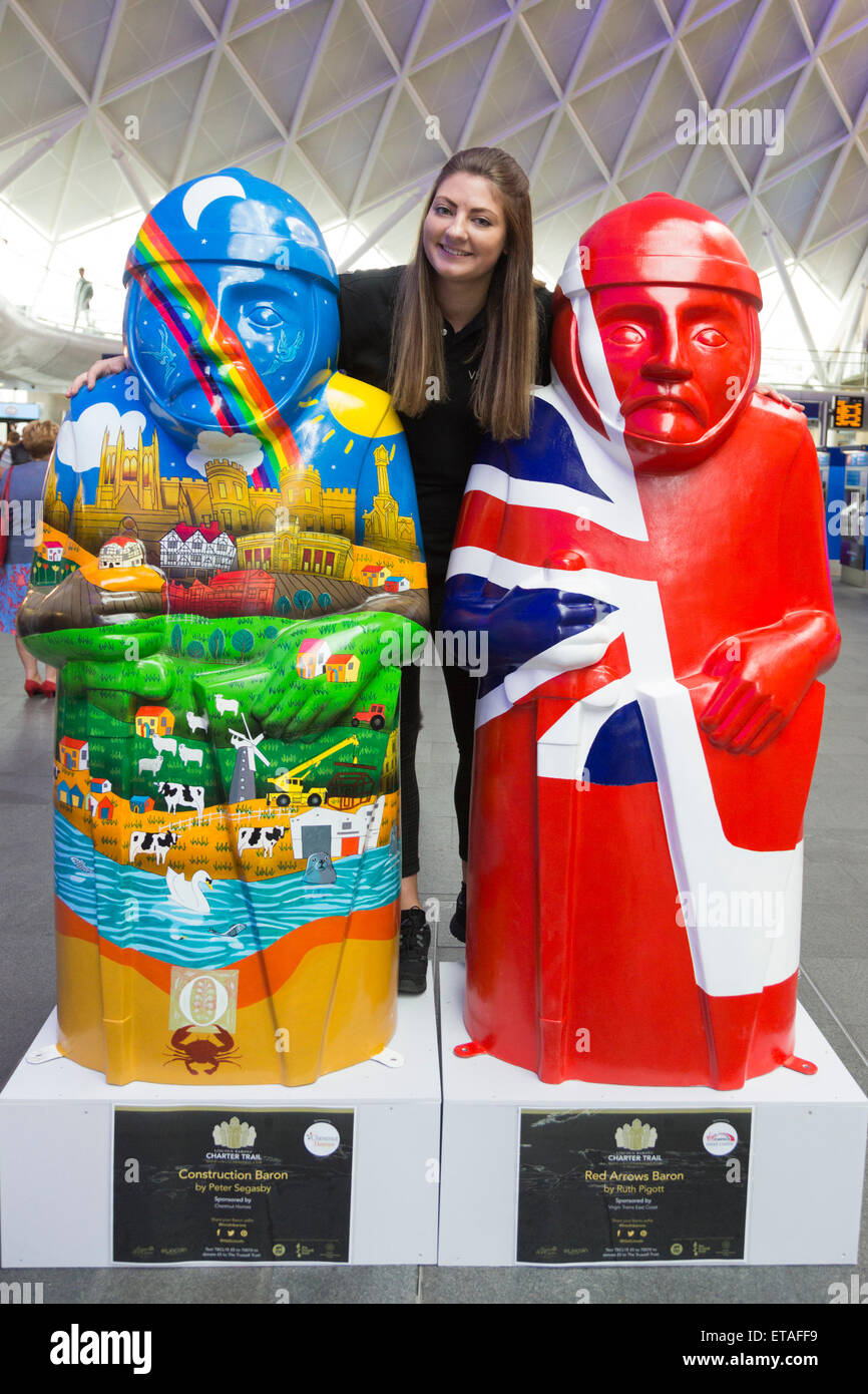 London, UK. Alison Grice, 22, of Visit Lincoln poses with the Lincoln Barons. Two Lincoln's Magna Carta Barons were today displayed at London's King's Cross Station before going back up to Lincoln tomorrow. Almost exactly 800 years since King John put his seal to Magna Carta, Lincoln is set to welcome a reincarnation of his 25 Barons into the city’s streets. The Lincoln Barons’ Charter Trail will see 25 2m-tall sculptures decorated by renowned artists from Lincolnshire and beyond.  Local businesses and organisations have worked with the artists to devise a different theme for each Baron. The t Stock Photo