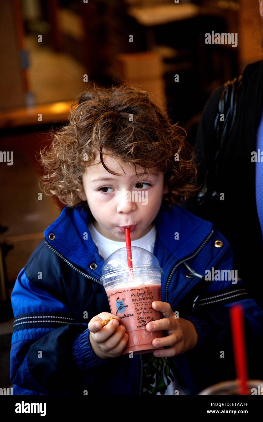 Young boy works at sipping his coffee house fruit smoothie through a