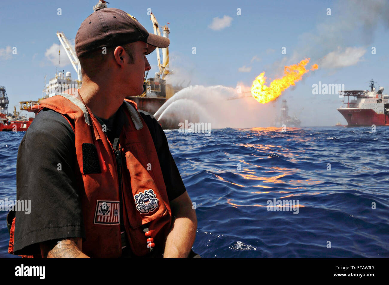 A Coast Guard officer watches the mobile offshore drilling unit Q4000 work to control the damaged Deepwater Horizon as crews work to plug the wellhead and flare excess gas and oil flowing from the well July 8, 2010 in the Gulf of Mexico. Stock Photo