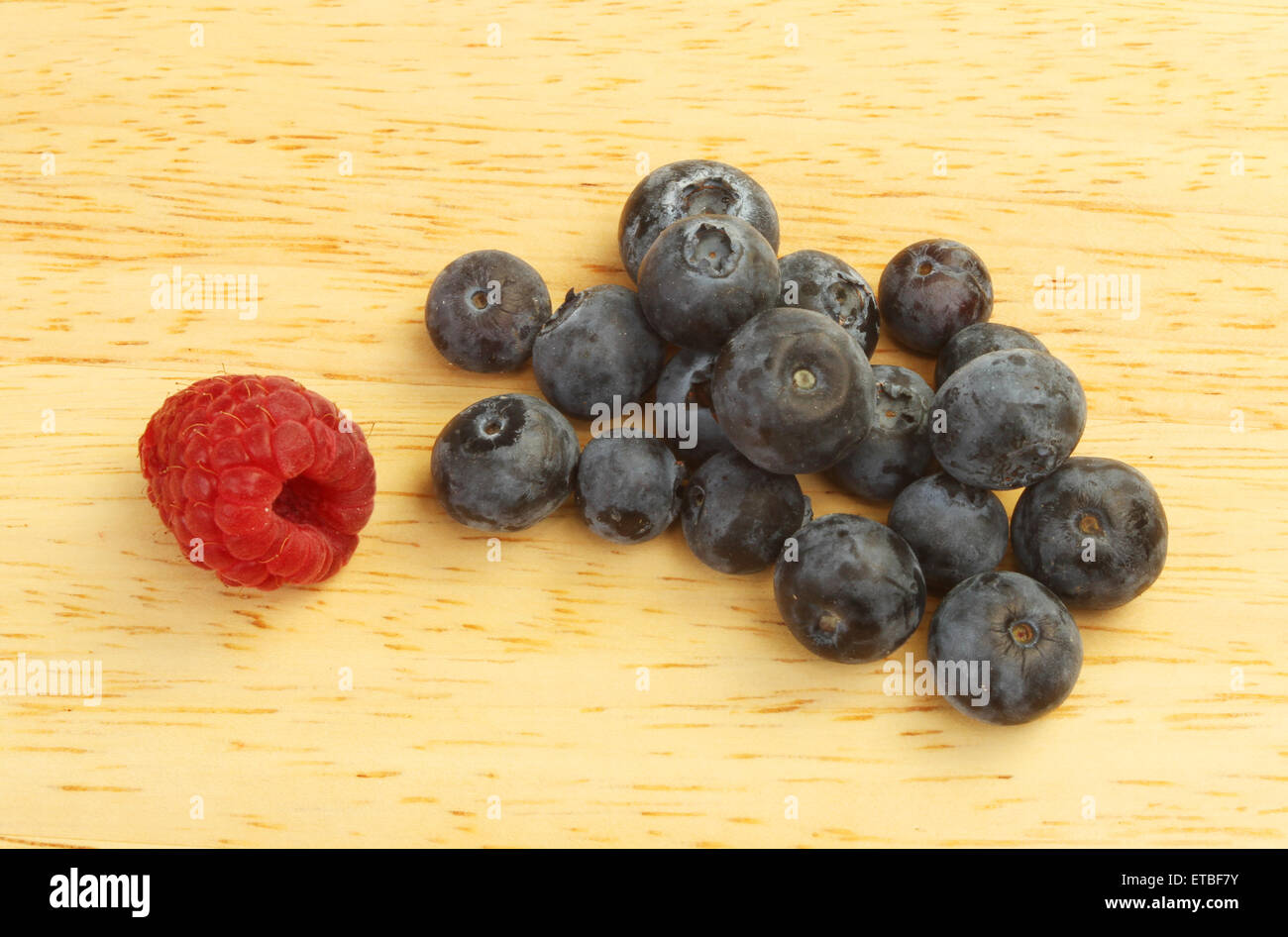 Blueberries and a single raspberry on a wooden board Stock Photo