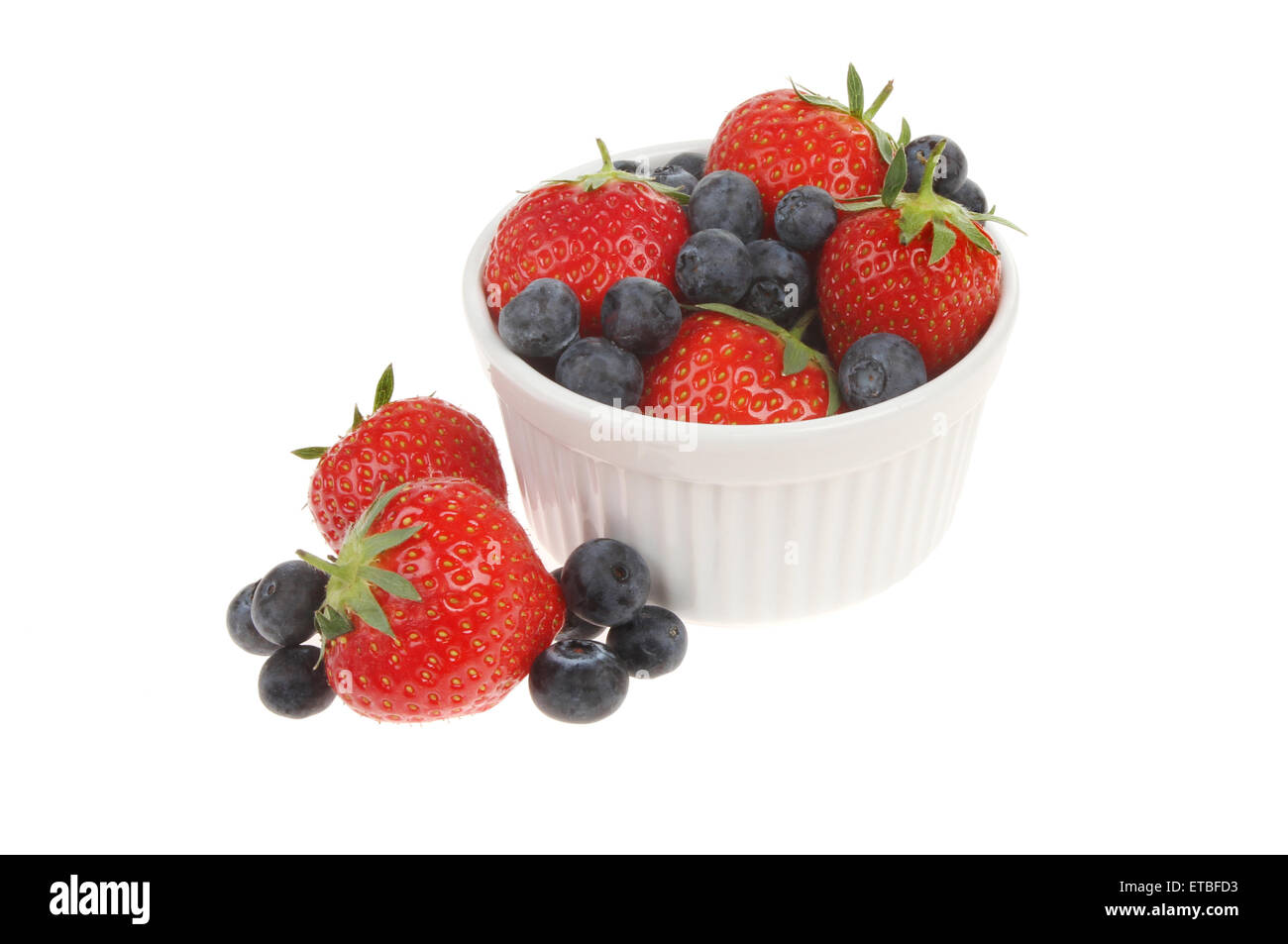 Strawberries and blueberries in and around a ramekin isolated against white Stock Photo