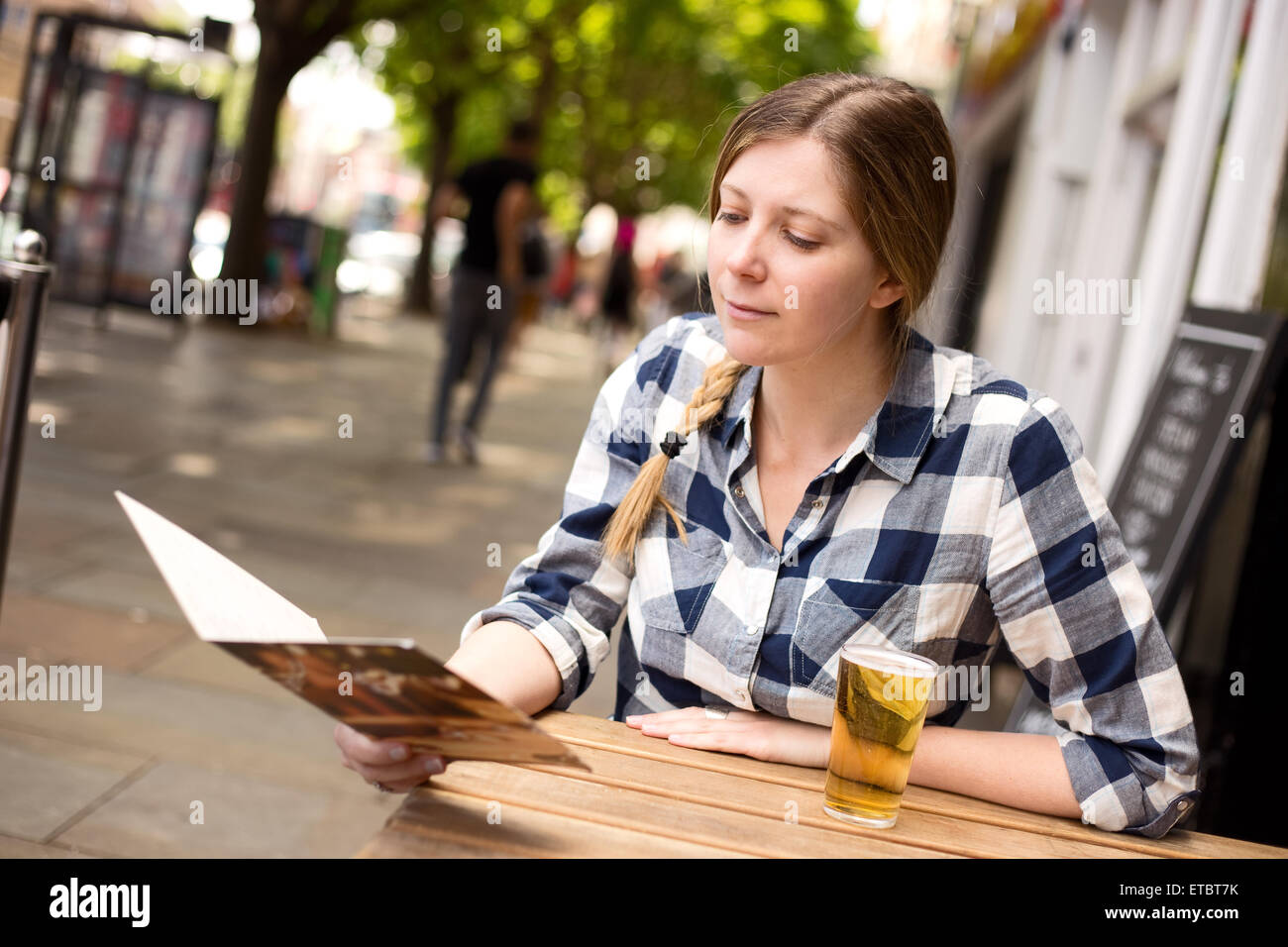 young woman sitting outside a bar with a drink and menu Stock Photo