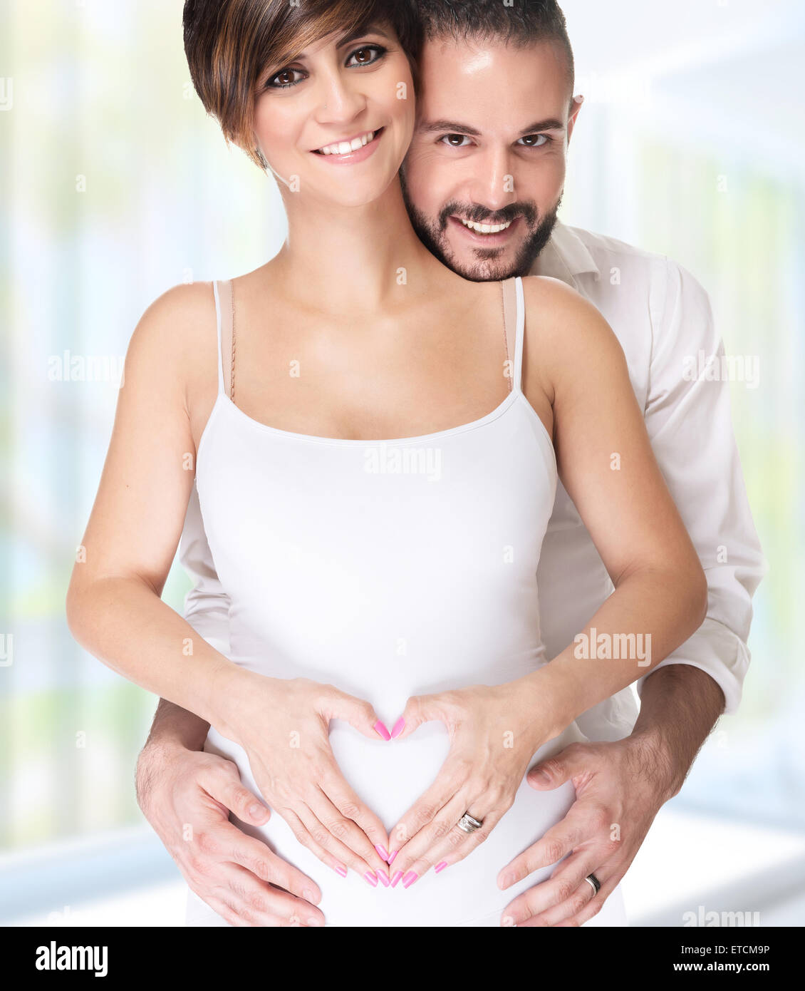 Portrait of beautiful happy couple holding hands in heart shape on the tummy, enjoying first pregnancy, happy young family Stock Photo