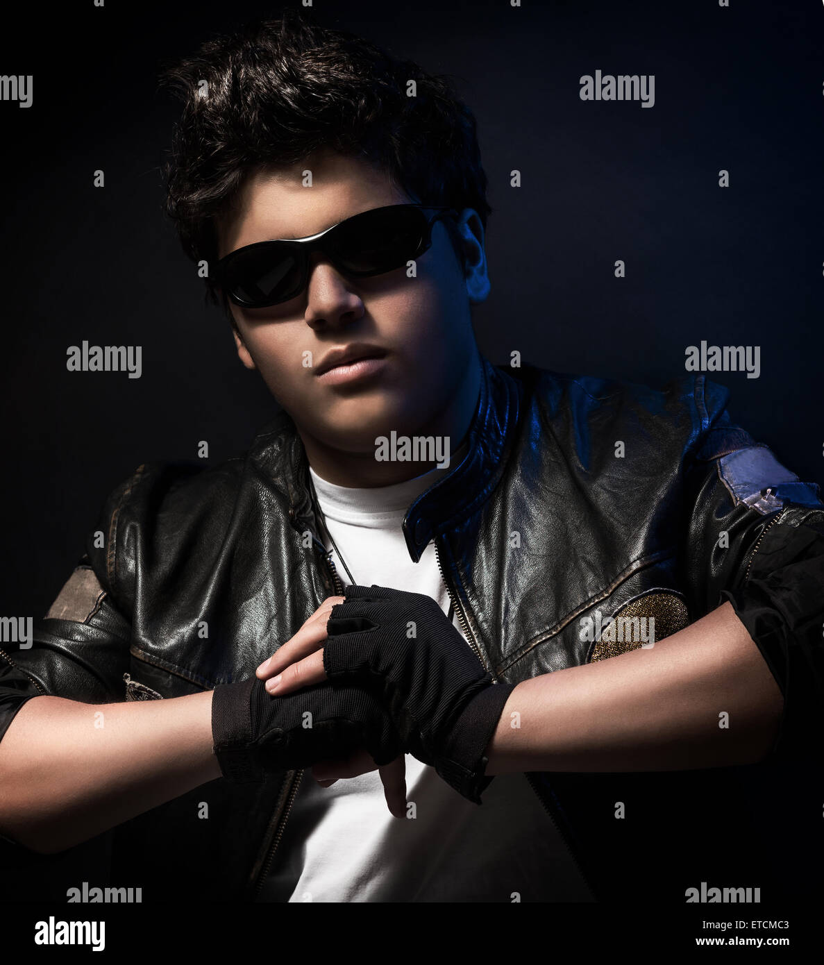 Handsome teen boy wearing stylish sunglasses and leather jacket over dark  red background, teenage fashion and style Stock Photo - Alamy