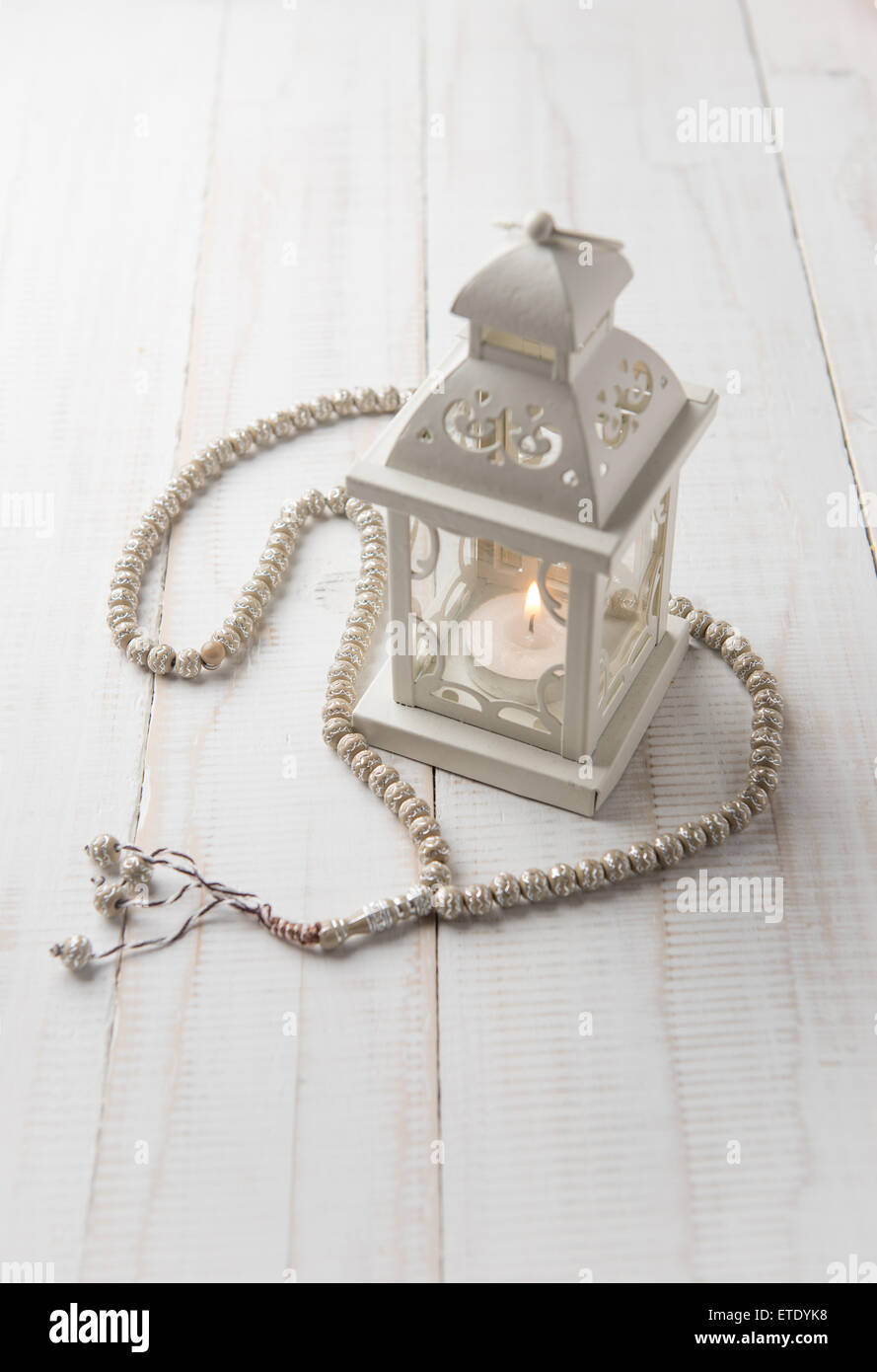 Small, white lamp with rosary on white background. Beautiful classic white candle holder. Stock Photo