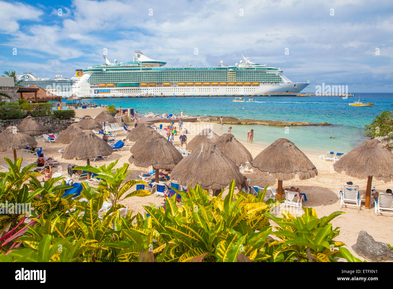 Liberty of the Seas cruise liner docked at Cozumel, Mexico. Tourists swimming and relaxing on the beach under cabanas. Stock Photo