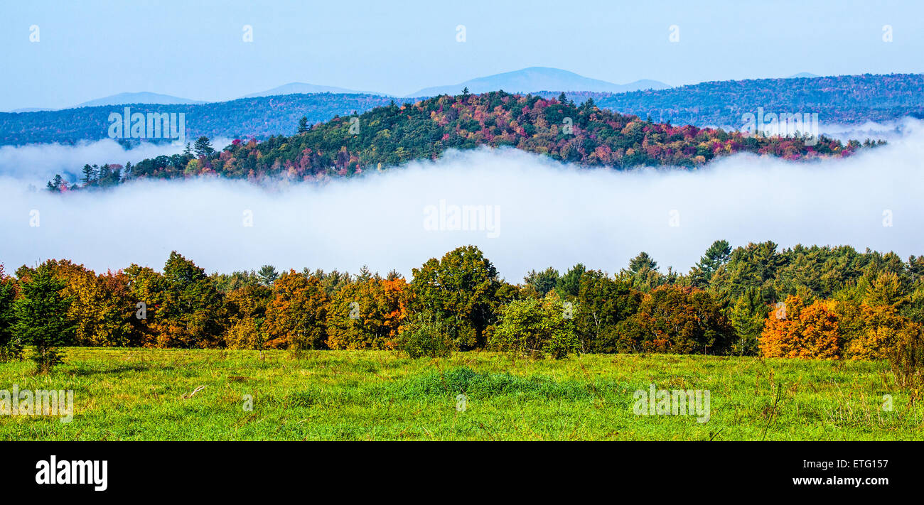 Small hill with colorful Autumn foliage with low morning mist appears as a floating island in Landaff, NH, USA. Stock Photo