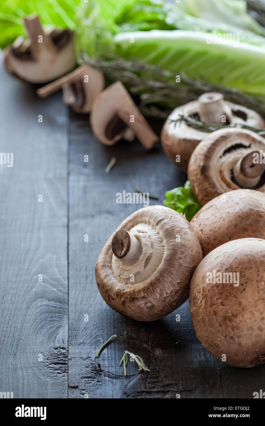 Fresh raw portobello mushrooms with rosemary and lettuce salad on wooden background Stock Photo