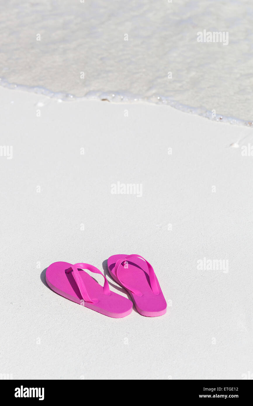 Pink flip flops on white sandy beach near sea waves, nobody. Summer vacation concept Stock Photo