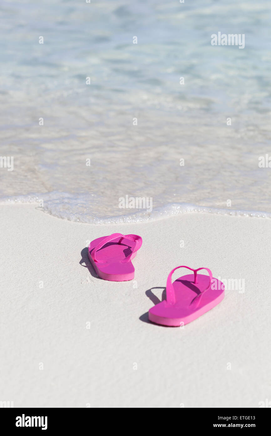 Pink flip flops on white sandy beach near sea waves, nobody. Summer ...