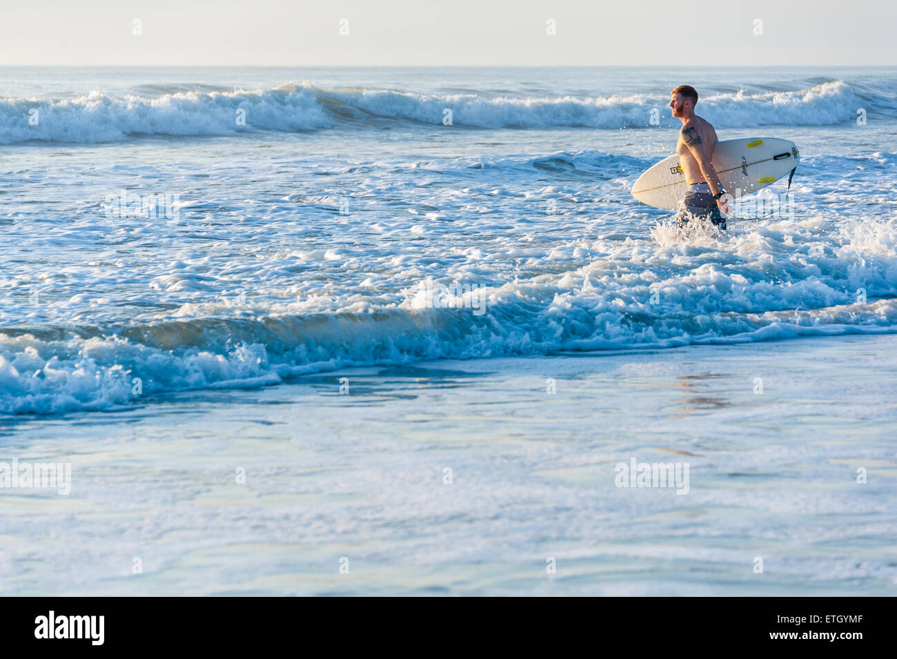 Florida surfer enters the ocean just after sunrise to catch some early morning waves at Jacksonville Beach. Stock Photo