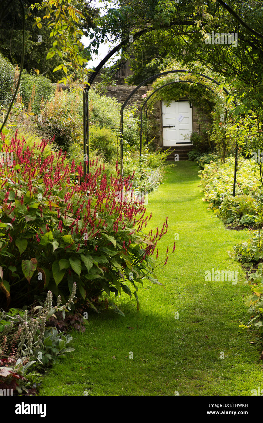 UK, England, Derbyshire, Eyam Hall garden, shady arbour leading to churchyard gate Stock Photo