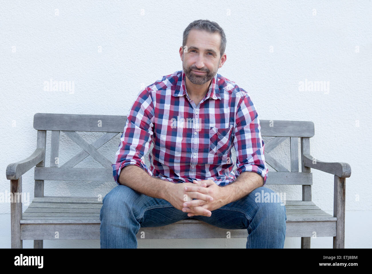 handsome man in his 40s in plaid shirt sitting on a bench Stock Photo