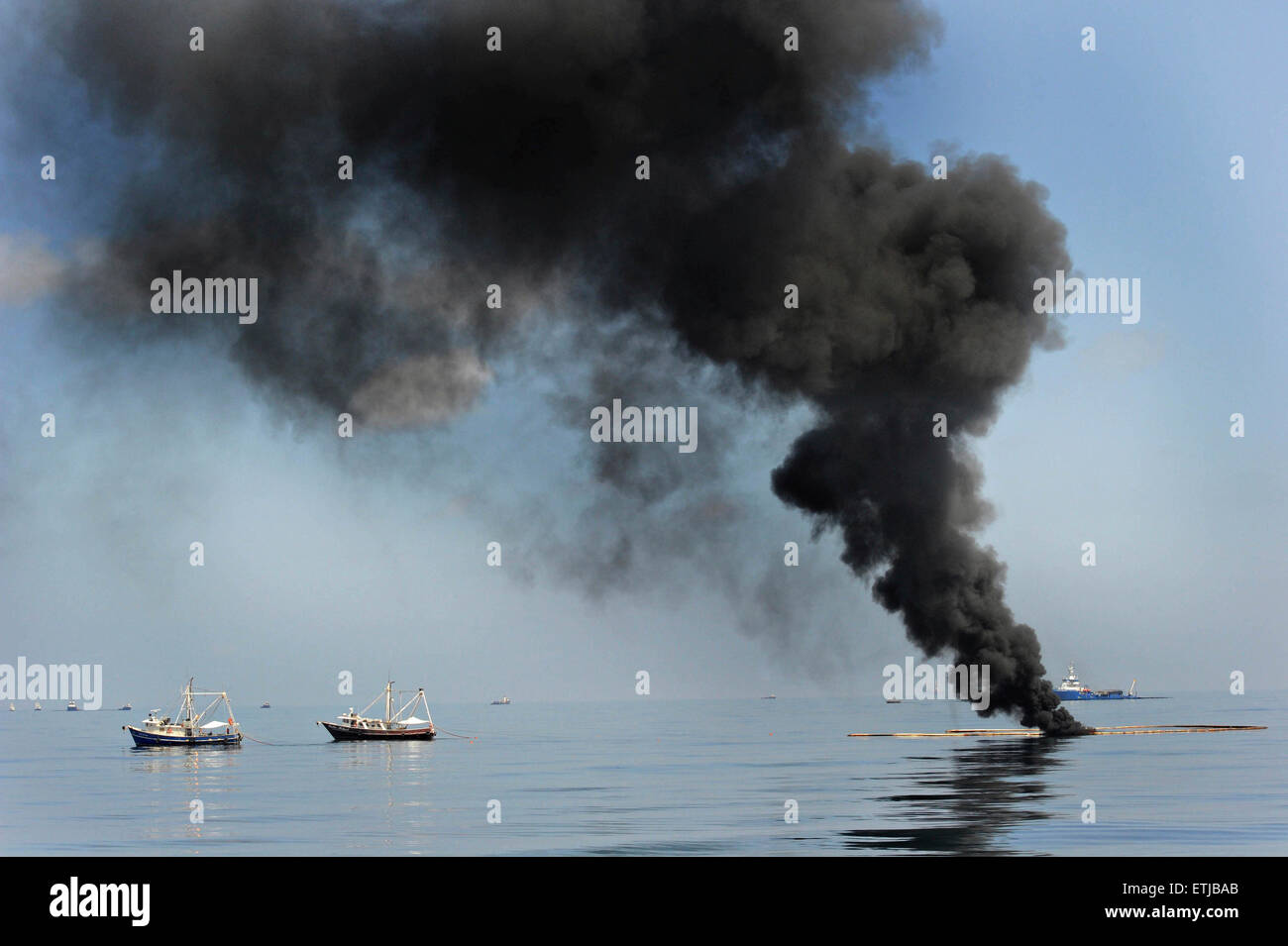 Dark clouds fill the sky as shrimp boats use a boom to gather crude oil during a controlled surface burn following the BP Deepwater Horizon oil spill disaster as efforts to contain and clean the millions of gallons of crew continue May 6, 2010 in the Gulf of Mexico. Stock Photo