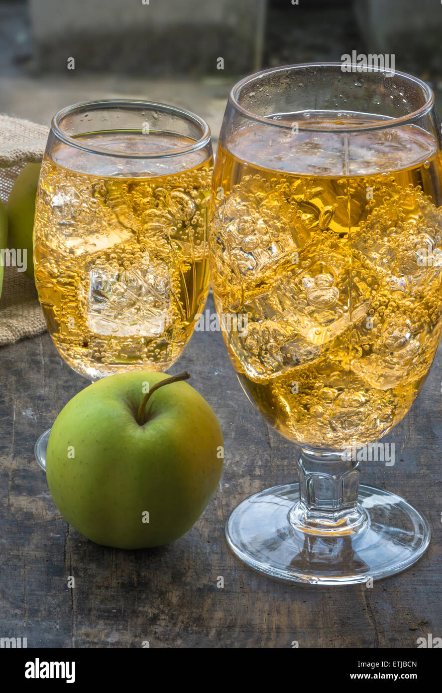 Glass of cold refreshing apple cider with ice cubes and apples on wooden table Stock Photo
