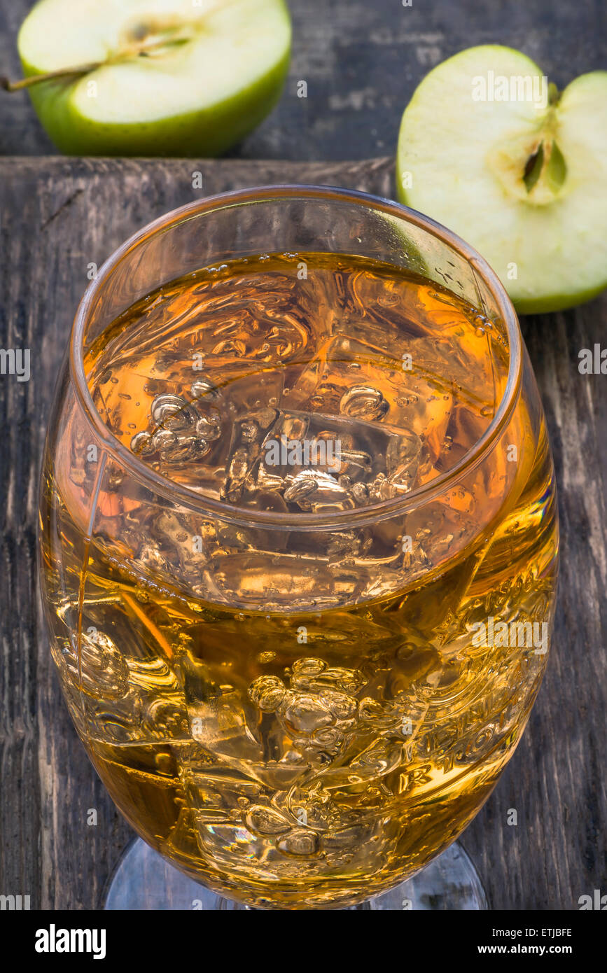 Glass of cold refreshing apple cider with ice cubes and apples on wooden table Stock Photo