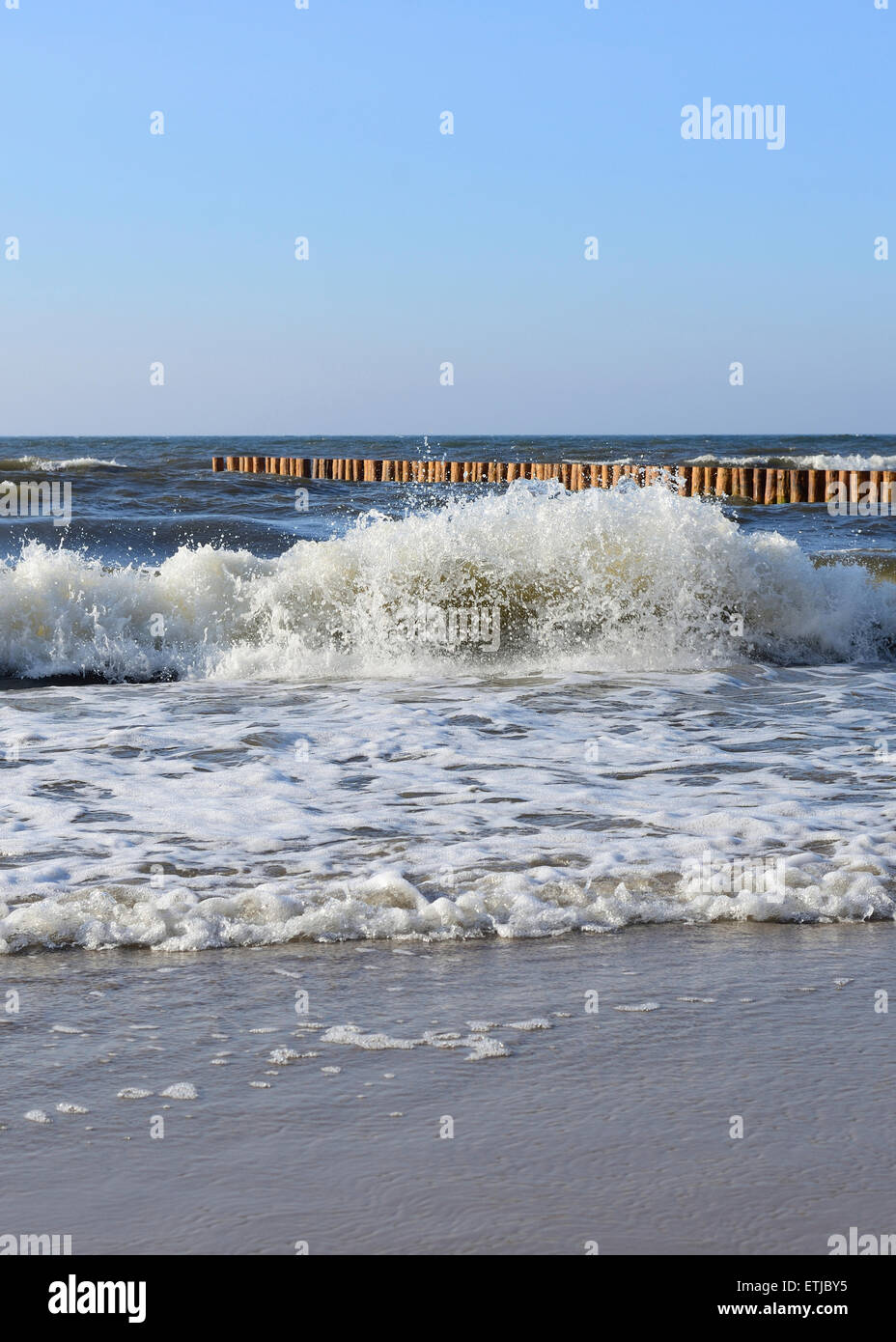 Waves on the beach with wooden wave breakers in the background Stock Photo