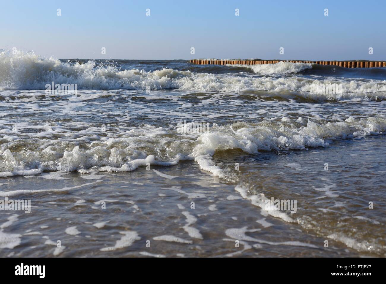 Waves on the beach with wooden wave breakers in the background Stock Photo