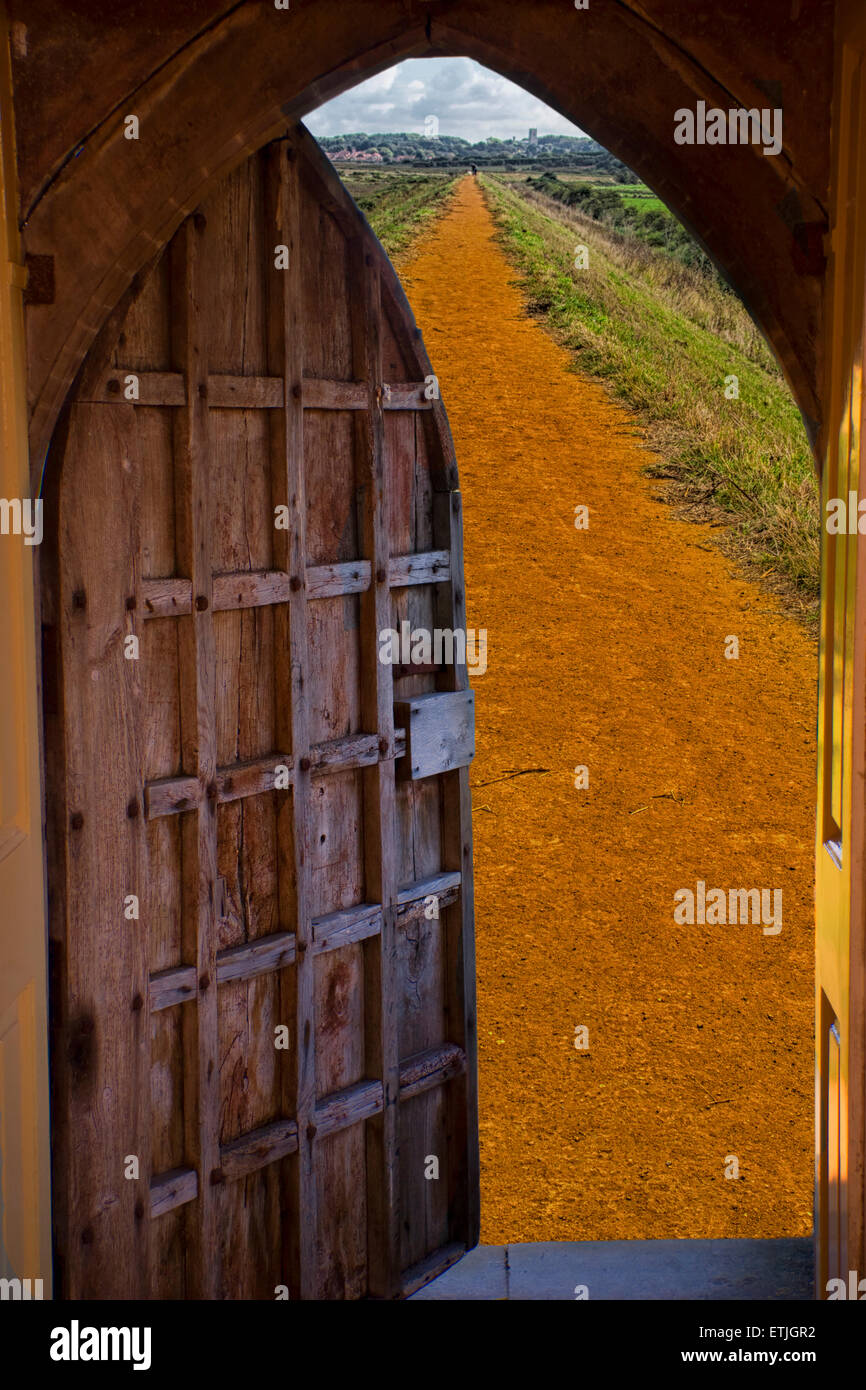 16th century heavy wooden door opening out onto a deserted straight dirt lane Stock Photo