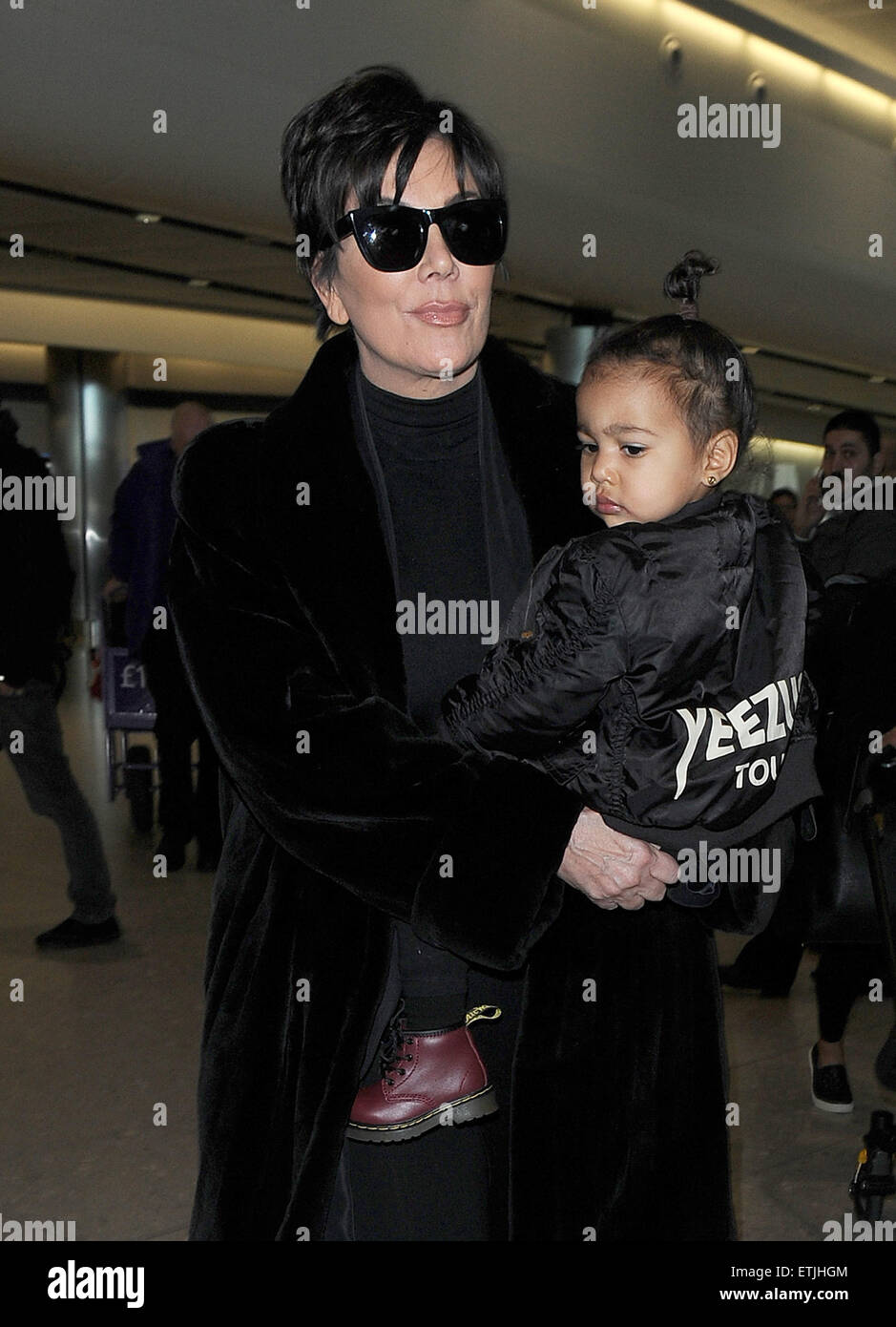 Kris Jenner, wearing a pair of Kanye West x Adidas Originals Yeezy 750 Boost,  arrives at Heathrow Airport carrying baby North West, who was wearing a 'Yeezus  Tour" bomber jacket in support