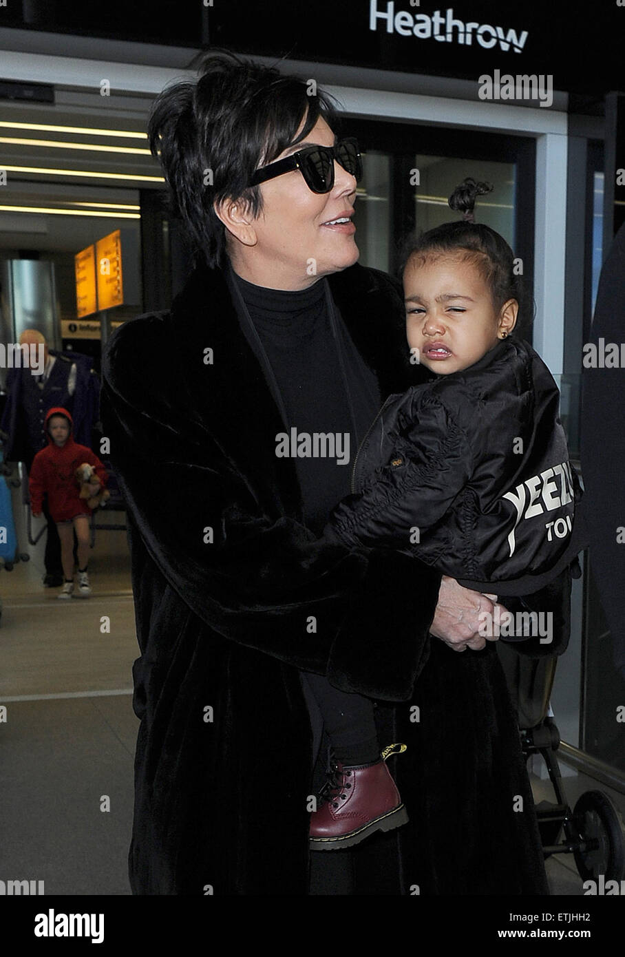 Kris Jenner, wearing a pair of Kanye West x Adidas Originals Yeezy 750 Boost,  arrives at Heathrow Airport carrying baby North West, who was wearing a  'Yeezus Tour